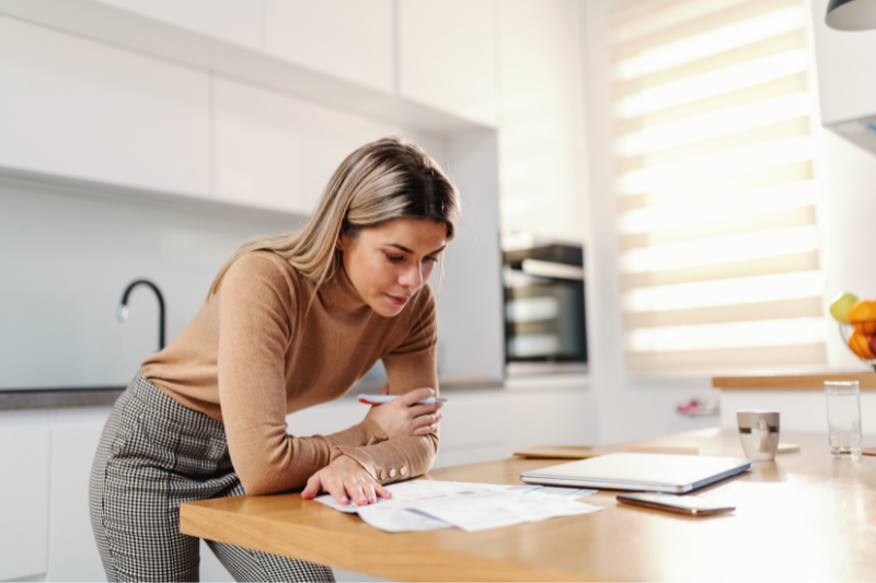 Woman standing in her kitchen looking over the documents.