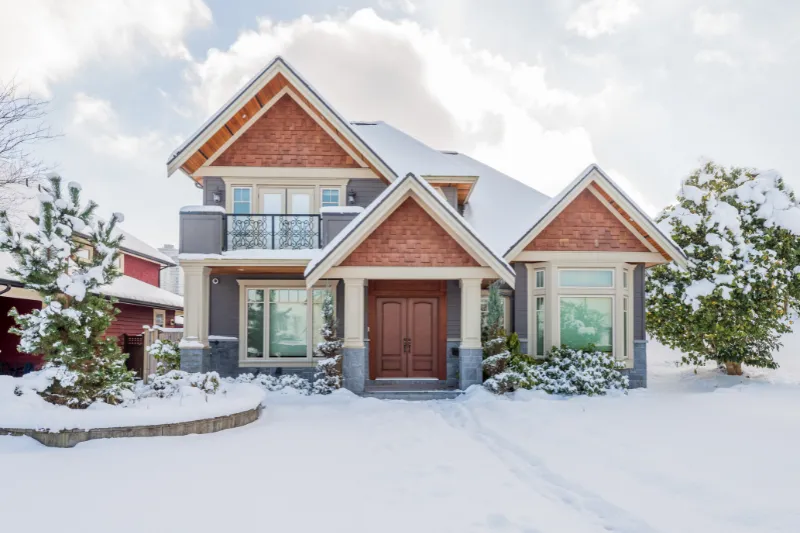 Front of a home in the winter surrounded by snow.