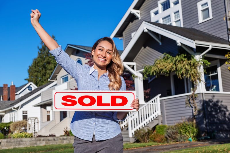 Real estate agent standing with SOLD sign in her hand.